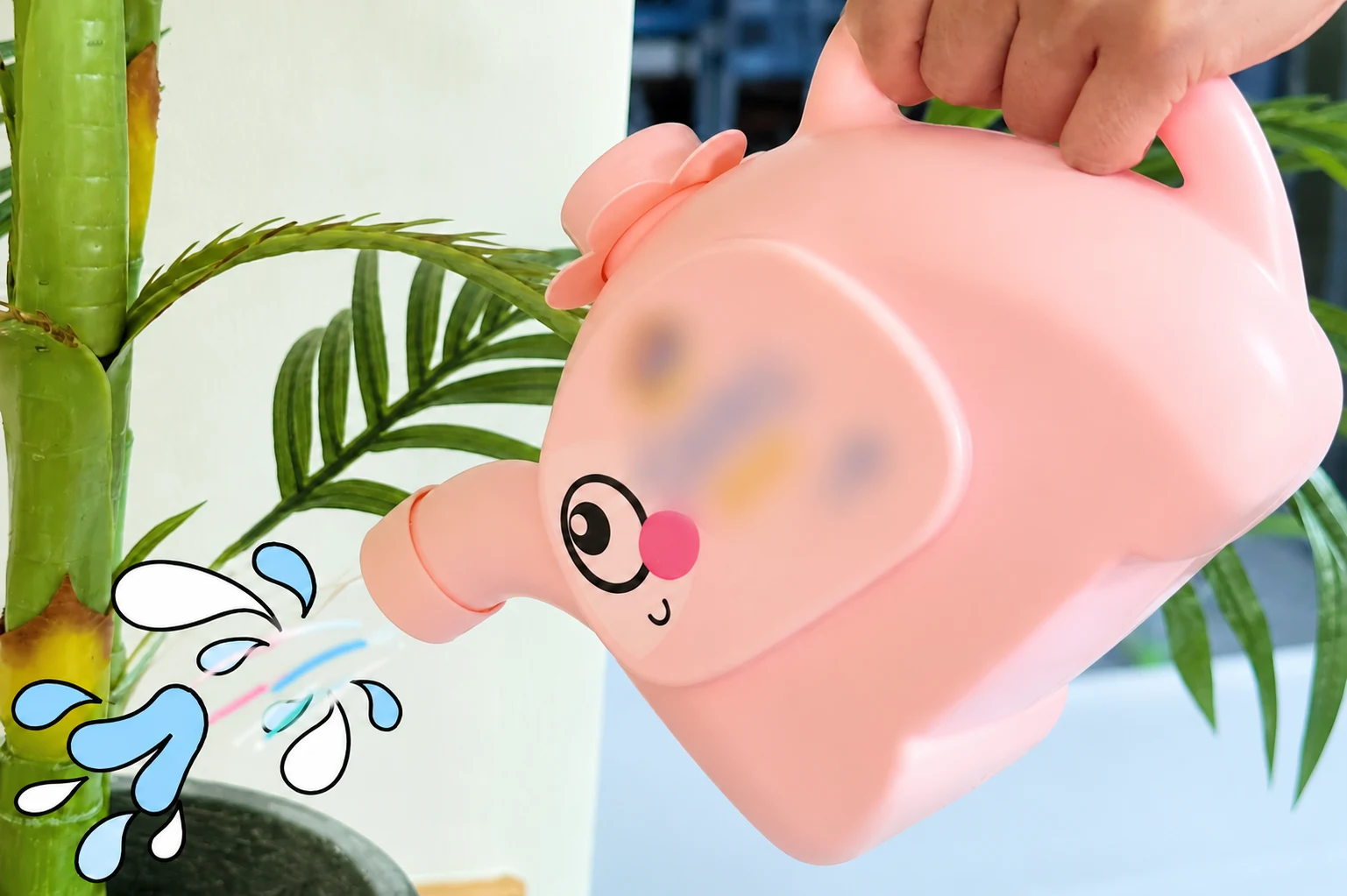 観賞用植物のそばでピンク色のじょうろ型容器を傾ける手。ブランド文字はぼかされ、水滴は描画されています。